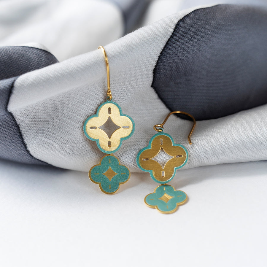 Gold and teal earrings on a white and gray fabric background